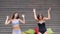 Laughing friends having fun on background wooden wall, girlfriends in bathing suits throw multi-colored cushion