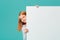 A laughing, happy Caucasian teenage girl looks out from behind an empty whiteboard. Empty space for your text, ads isolated on a