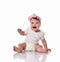 Laughing little baby infant girl in white body and hair bow decoration sits on floor looking at camera waving with hand