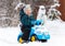 Laughing little boy drives toy car on snow