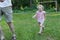 Laughing little daughter running after her father in summer park outdoors