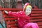 Laughing little girl leaning forward and sitting on red rest wood bench