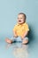 Laughing loud infant baby child boy toddler in blue jeans and yellow polo shirt is sitting on the floor