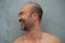 Laughing profile of 30-40s beard bald Japanese topless happy cool man portrait on grey concrete wall background