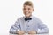 A laughing schoolboy in a blue shirt with a bow tie sits at the table. Back to school. White background