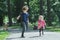 Laughing sibling children playing tag and running on park asphalt footpath