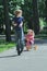 Laughing sibling sister chasing after her brother on pink and yellow kids tricycle