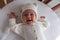 Laughing smiling cute 2 month old baby girl in a white hat lies in a white round crib