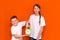 Laughing young caucasians two friends guy and girl in white empty blank design t-shirts posing on orange studio wall