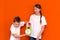 Laughing young caucasians two friends guy and girl in white empty blank design t-shirts posing on orange studio wall