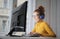 Laughing young female with glasses and headphones sitting in front of the computer in the house