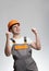 Laughing young foreman in hardhat and overalls rejoices on grey studio background