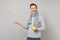 Laughing young man in gray sweater, scarf holding throwing up lemons on grey background in studio. Healthy