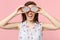 Laughing young woman holding, covering eyes with halfs of fresh ripe pitahaya dragon fruit isolated on pink pastel wall