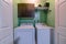 Laundry appliances inside the small room of a house with wall cabinet and shelf