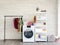 Laundry room interior with washing machine and colorful clothes on white vintage brick wall background