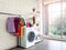 Laundry room interior with washing machine and colorful clothes on white vintage brick wall background