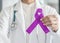 Lavender purple cancer all kinds awareness ribbon on doctor`s hand support for national cancer survivor month charity campaign