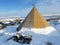 A Lavvu, a Sami people`s tent in thick snow, snowmobiles and transport vehicles. Polar extreme temperature