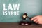 Law is true. Court hammer in man& x27;s hand on a wooden table. Green chalk board