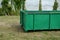On the lawn is a green tin container for grass clippings from gardens and parks. a man checks the quality and quantity of grass by