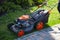 Lawn mower mows grass on the lawn. Street on a sunny summer day in the park