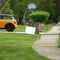 Lawn sign near driveway with yellow car