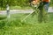 Lawnmower mowing high green grass on the lawn in the park