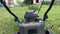 A lawnmower riding along a green grass field, mowing lawn and garden chores in summer, backyard care