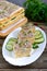 Layer cake with eggs, cheese, green onions, canned fish, mayonnaise on a white plate on a wooden table. Festive appetizer