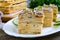 Layer cake with eggs, cheese, green onions, canned fish, mayonnaise on a white plate on a wooden table. Festive appetizer. Close-