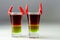 Layered drink shot prepared with vodka, green liquor, grenadine and lemon juice decorated with bird eye chillies in the shape of