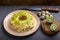 Layered salad with chicken and kiwi next to quail eggs kiwi and a knife on a gray table.