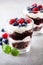 Layered trifle dessert with chocolate sponge cake, whipped cream, berries and fruit jelly in serving glasses