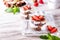 Layered trifle dessert with sponge cake, whipped cream and strawberries in serving glasses on a white wooden background