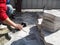 Laying gray paving tiles `Bikini` in the yard. There are part of the body of a man with a rubber hammer in his hand and a stack