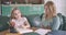 Lazy Caucasian girl sitting at the table having no wish to study. Young mother trying to help daughter doing homework