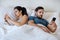 Lazy couple ignoring themselves lying in bed and holding smartphone