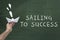 Leadership, business, success concept. Human hand holding paper boat against green blackboard with text: Sailing to success.