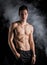 Lean athletic shirtless young man standing on dark background