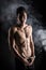 Lean athletic shirtless young man standing on dark background