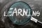 Learn, study and inspect learning - pictured as a magnifying glass enlarging word learning, symbolizes researching, exploring and