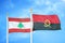 Lebanon and Angola  two flags on flagpoles and blue cloudy sky