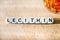 Lecithin gel pills in a round glass bowl and with the word Lecetin from the letters of cubes on a light wooden background. Soy