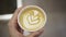 Left hand holding a paper cup of Latte coffee with tulip latte art