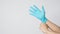 Left hand is pulling right hand wearing blue latex gloves on white background