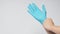 Left hand is pulling right hand wearing blue latex gloves on white background