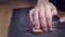 Left handed man cutting the fat off slices of bacon with big kitchen knife on black board on wooden kitchen table