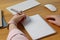 Left-handed woman writing in notebook at wooden desk, closeup