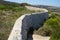 A leg protruding from a hole in the wall that is located along the perimeter of Fort Campbell. Selmun, Mellieha, Malta.